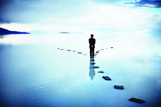 A figure walking on a path of stones through water and reaches as fork