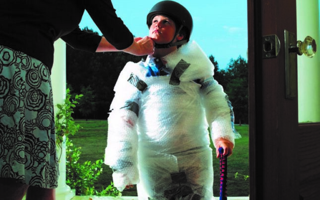 A parent wrapping their child in bubble wrap and helmet