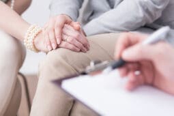 A couple holds hands as a therapist takes notes