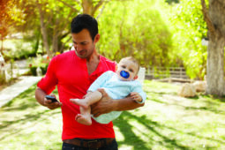 A man holds a baby in one hand and looks at his phone in another