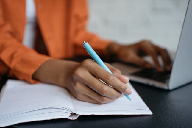 A person holding a pen to a notebook