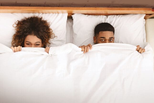 Two people in bed hiding under the covers