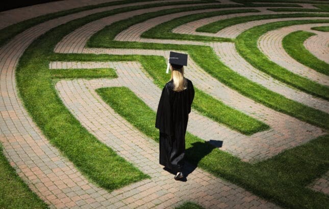 A woman in academic regalia walks a labyrinth