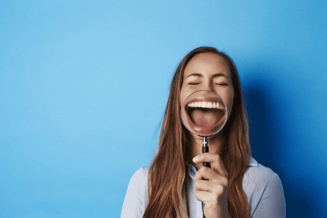 A woman holds a magnifying glass over her smile