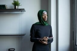 Black woman with a head scarf stares out the window - Photo Credit: Pexels/Monstera