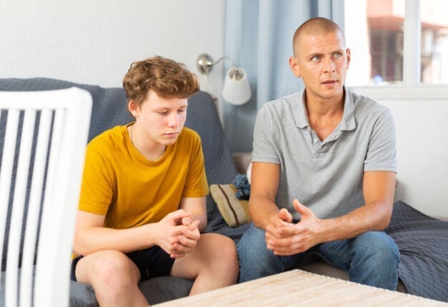 Teenage son and father sitting on a couch / iStock