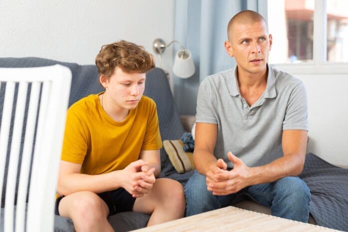 Teenage son and father sitting on a couch / iStock