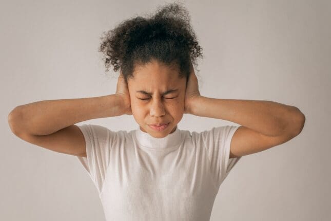 Black teen girl putting her hands over her ears | Photo by Monstera