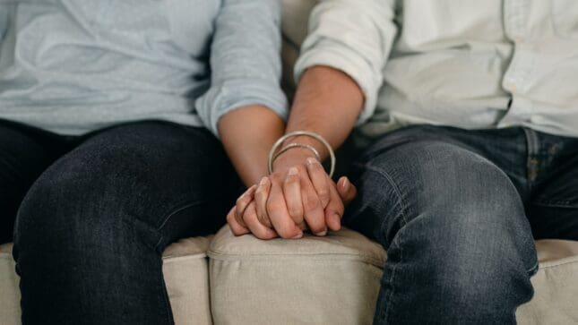 Two people holding hands on a couch | Photo by Ketut Subiyanto/Pexels