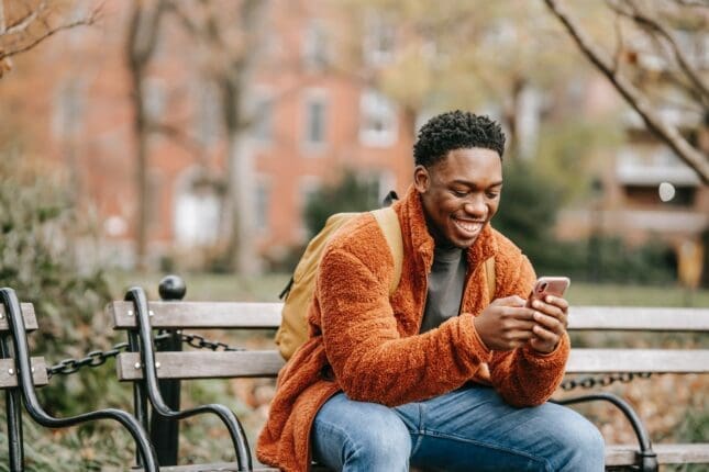 Happy man on a park bench looking at his phone | Photo by Keira Burton/Pexels