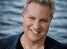 Grey-haired man smiling in front of water in a blazer