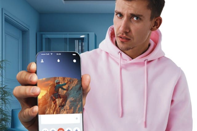 A man in a pink hoodie holds a phone toward the camera's view, showing a dating app profile