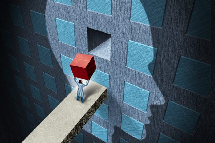 The outline of a head is projected on a wall with a small man lifting a block to fit it into the missing piece of the wall