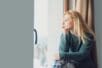 A woman looks out a window, thoughtful and sad