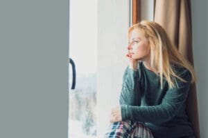 A woman looks out a window, thoughtful and sad