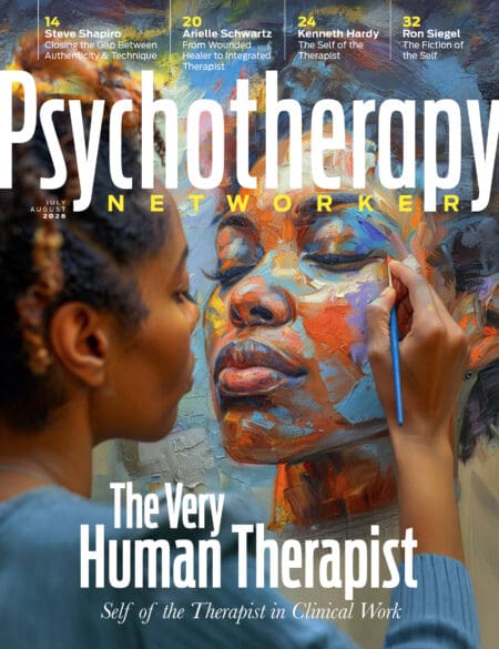 A woman holds a paintbrush, painting in her own face