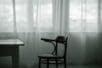 An empty chair sits in front of windows covered in light fabric